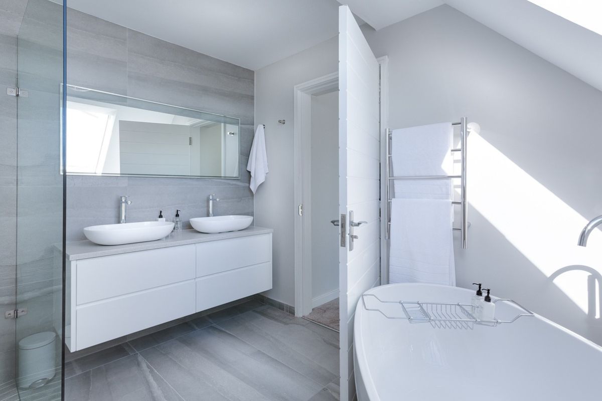 this white minimalist bathroom essentials for a holiday let property, two sinks, under sink storage, walk in shower and separate bath. Heated towel rack too.