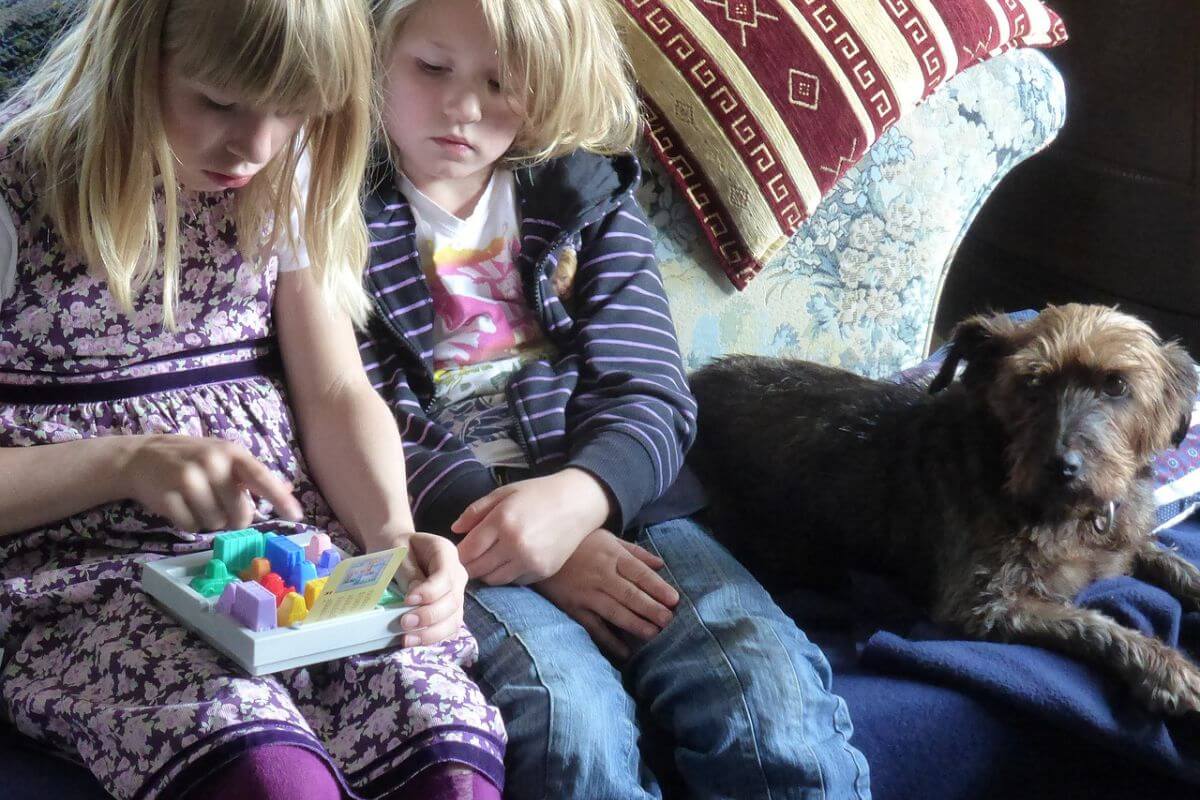 children playing with a puzzle on the sofa with their brown dog in a holiday home